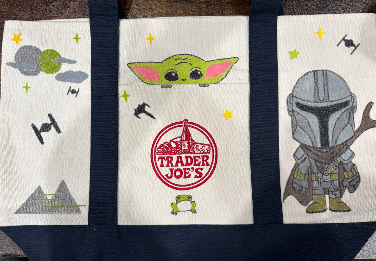 Space Friends hand painted tote with a green foundling peeking from the pocket and a chibi armored bounty hunter