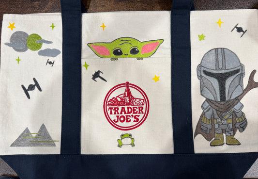 Space Friends hand painted tote with a green foundling peeking from the pocket and a chibi armored bounty hunter