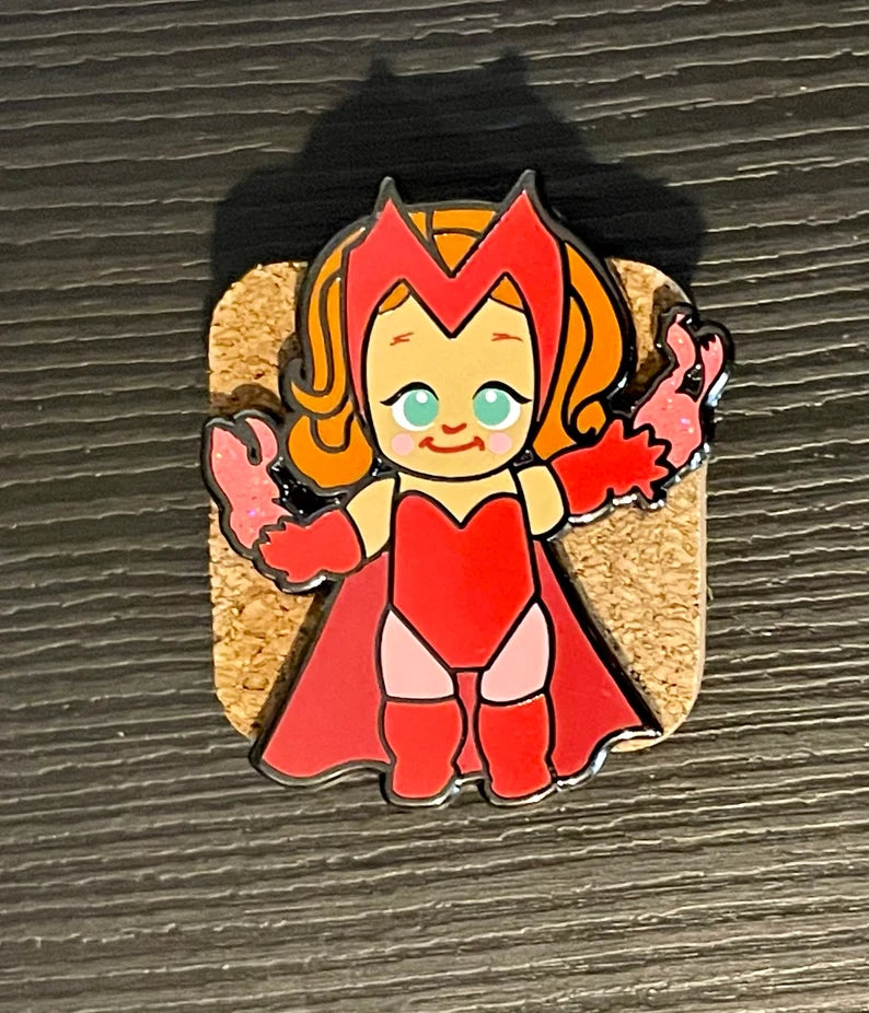 Red Magic Woman chibi enamel pin, green eye variant, with glitter pink hex magic on a cork board